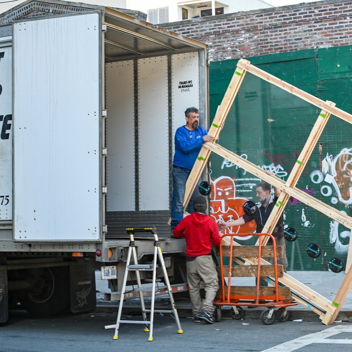 Professional movers carefully unloading a large wooden-framed item from a moving truck during a heavy furniture move in La Jolla, CA.